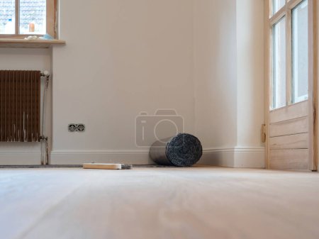 Photo for Expansive apartment room during renovation, featuring wooden floors covered with gray malervlies painters fleece for protection against painting and work. - Royalty Free Image