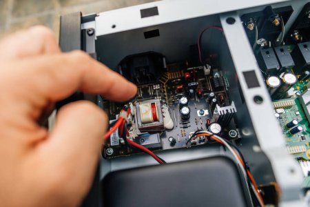 Foto de Una mano masculina prueba y repara meticulosamente un potente amplificador de música, centrándose en múltiples condensadores y componentes. - Imagen libre de derechos