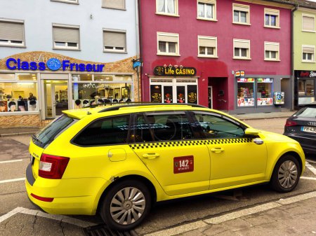 Photo for Kehl, Germany - Dec 21, 2023: cultural blend as a Romanian yellow Skoda taxi stands parked in a German city, juxtaposed against the backdrop of a bustling casino and a trendy haircut salon. - Royalty Free Image