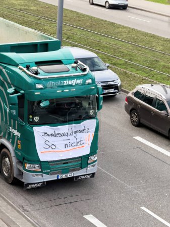 Photo for Kehl, Germany - Jan 9, 2024: green truck driving slowly through shut down roads in Kehl, Germany, as part of a protest against greener farming policies. A placard is displayed on the white curtain in - Royalty Free Image