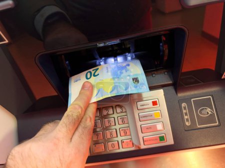 Téléchargez les photos : Récupérer les billets de 20 euros du distributeur automatique, capturant la commodité et la facilité d'accès à l'argent sur demande. - en image libre de droit