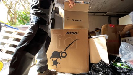 Téléchargez les photos : Paris, France - 8 août 2023 : Une main masculine ouvre une barre Stihl dans son garage, se préparant au jardinage printanier avec plusieurs boîtes prêtes à déballer. - en image libre de droit