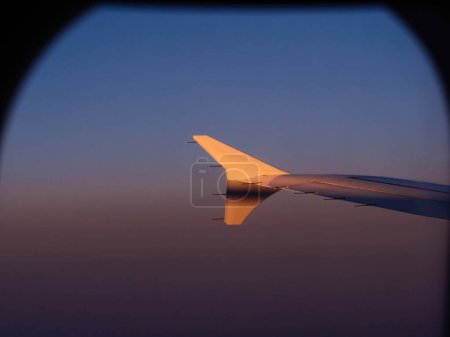 Airplane wing visible through window with a serene evening blue cast, evoking a sense of travel to a distant destination