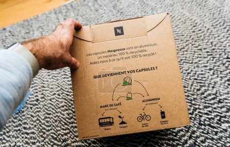 Téléchargez les photos : Brême, Allemagne 10 Déc 2023 : Une main masculine se prépare à déballer la boîte à capsules de café Nespresso, en réfléchissant : Que deviendront vos capsules après recyclage Promouvoir la conscience environnementale - en image libre de droit