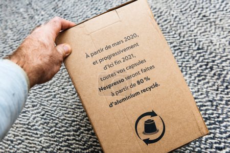 Photo for Bremen, Germany Dec 10, 2023: POV A male hand reads on the cardboard box that starting March 2020 until 2021, all Nespresso capsules from the Swiss brand will be made from 80percent aluminum, ensuring - Royalty Free Image