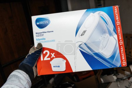 Photo for Bremen, Germany Dec 10, 2023: A gloved male hand holds the Marella Brita water filter cartridge box, ensuring hygiene and cleanliness in handling water filtration essentials - Royalty Free Image