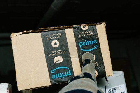 Photo for Bremen, Germany - Dec 10, 2023: A warehouse worker wearing a glove is pointing to the Prime logo on an Amazon Prime cardboard package, illustrating the concept of working and delivering parcels - Royalty Free Image