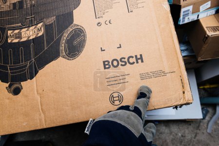 Foto de Bremen, Alemania - 10 de diciembre de 2023: Una mano de obra que lleva un guante señala el logotipo de Bosch en una aspiradora industrial profesional hecha en Italia, con varios idiomas, destacando el unboxing - Imagen libre de derechos