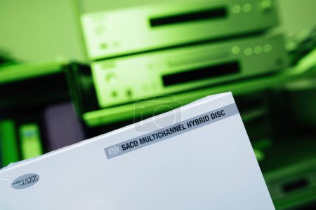Foto de El paquete de un nuevo SACD con música de jazz de alta definición se exhibe sobre un fondo verde vívido, con un sistema de alta fidelidad desenfocado en el fondo - Imagen libre de derechos