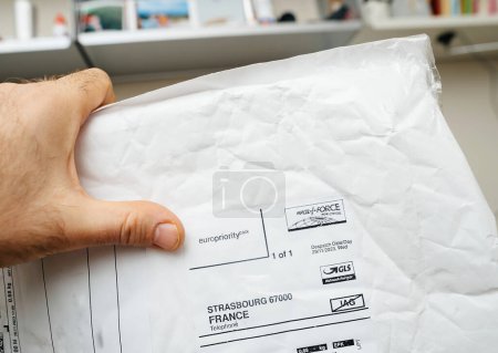 Photo for Paris, France - Dec 28, 2023: An arm holds an envelope featuring the logos of Parcel Force Worldwide and GLS, indicating a UK to Europe delivery partnership - Royalty Free Image