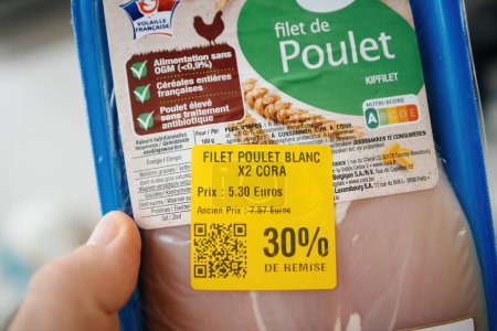 Téléchargez les photos : Paris, France - Jan 12, 2024 : Du point de vue POV, une main masculine tient un filet de poulet Auchan étiqueté Nutri-Score A, avec une réduction spéciale de 30 % en raison de son expiration prochaine - en image libre de droit