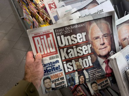 Photo for Kehl, Germany - Jan 9, 2024: A person is captured in the act of picking up a newspaper with a headline mourning the loss of Franz Beckenbauer a prominent figure, symbolizing a moment of collective - Royalty Free Image