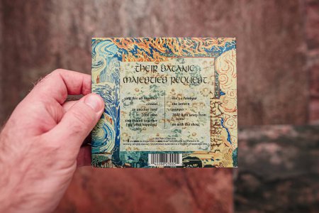 Photo for Paris, France - Jan 12, 2024: Against a vibrant red background, a male hand delicately holds the luxury packaged vintage SACD of Their Satanic Majesties Request, an iconic album, exuding timeless - Royalty Free Image