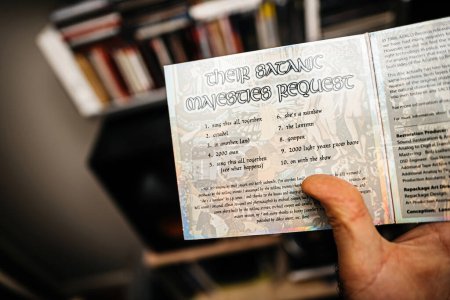 Photo for Paris, France - Jan 12, 2024: A male hand holds The Rolling Stones Their Satanic Majesties Request SACD, displaying the tracklist. Vitsoe shelves form the background - Royalty Free Image