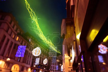 Téléchargez les photos : Un éclair vert et jaune vibrant traverse un ciel crépusculaire au-dessus de décorations festives de rue illuminées dans un cadre urbain pittoresque - en image libre de droit