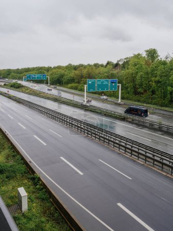 Foto de Frankfurt, Alemania - 4 de mayo de 2019: Una autopista húmeda con pocos coches, bordeada de vegetación, bajo cielos nublados. - Imagen libre de derechos