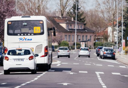 Foto de Haguenau, Francia - 20 de marzo de 2024: Una bulliciosa calle en Haguenau cuenta con un autobús escolar y coches que conducen a lo largo de la carretera, que representan la vibrante vida cotidiana y la dinámica de transporte de la ciudad.. - Imagen libre de derechos