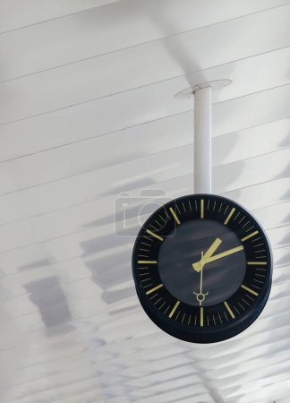 Photo for A clock is suspended from the ceiling in a train station platform showing the time to passengers below - Royalty Free Image