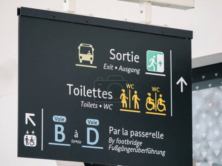 Multilingual signage at a train station displaying directions for exits, toilets, and platforms in French, English, and German