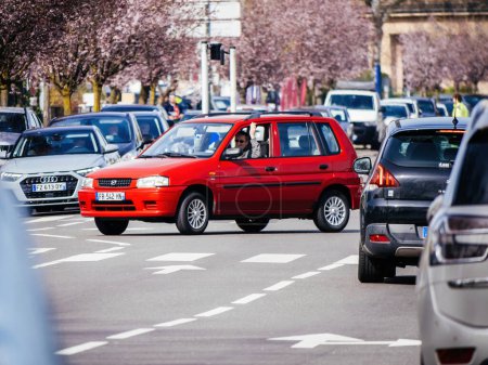 Téléchargez les photos : Haguenau, France - 20 mars 2024 : Voiture Peugeot rouge naviguant à travers la circulation dans la ville de Haguenau, entourée de divers autres véhicules dans une rue animée - en image libre de droit