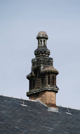 Ein detaillierter Steinkamin ziert ein Dach im elsässischen Haguenau und zeigt die traditionelle Architektur der Region vor klarem Himmel
