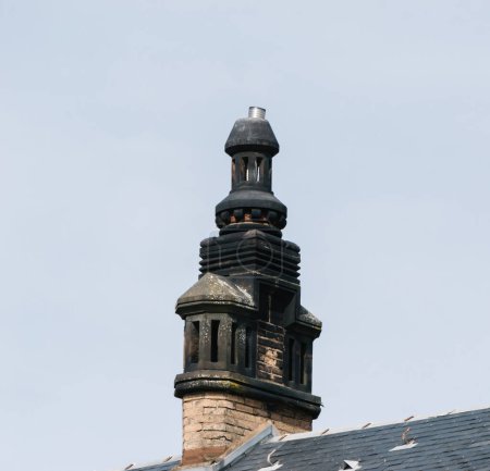 Téléchargez les photos : Une cheminée en pierre détaillée se dresse fièrement sur un toit à Haguenau, en Alsace, mettant en valeur l'architecture intemporelle des régions dans un contexte de ciel clair - en image libre de droit