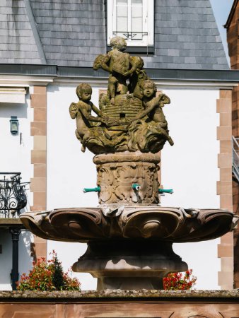 Photo for A serene fountain stands gracefully in front of a pristine white building, exuding elegance and charm - city of Haguenau, Alsace, France - Royalty Free Image