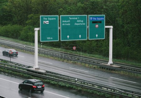 Téléchargez les photos : Francfort, Allemagne - 4 mai 2019 : Les routes humides conduisent les voyageurs à franchir les panneaux directionnels pour The Squaire et le terminal 1 de l'aéroport de Francfort par temps couvert et pluvieux - en image libre de droit