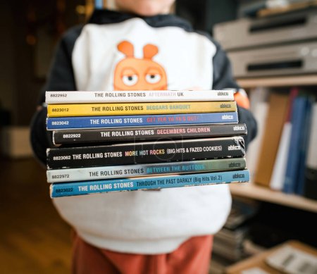 Photo for Frankfurt, Germany - Jan 12, 2024: A small child holds a stack of The Rolling Stones albums, partially obscuring their face, in a charming display of early music appreciation. - Royalty Free Image