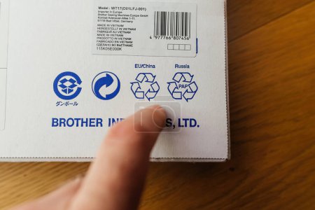 Téléchargez les photos : Paris, France - 9 mars 2024 : Gros plan d'une main masculine pointant vers des logos de recyclage pour l'UE, la Chine et la Russie, ainsi que l'étiquette importée et l'étiquette Made in Vietnam sur la table à coudre Brother - en image libre de droit