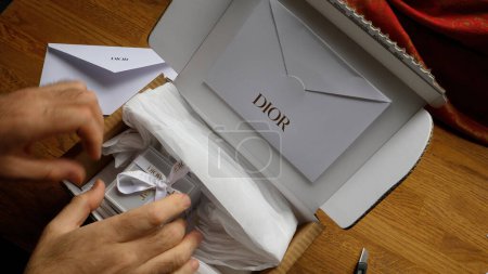 Foto de París, Francia - 5 de junio de 2020: Manos delicadamente desempaquetar un artículo de lujo de Dior, mostrando el elegante embalaje y la anticipación de revelar un producto de alta gama - Imagen libre de derechos