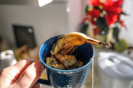 Téléchargez les photos : Une tasse bleue regorge de pelures de fruits, un effort personnel pour composter les déchets de cuisine à la maison, présenté dans un cadre ensoleillé - en image libre de droit