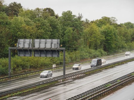 Frankfurt, Deutschland - 4. Mai 2019: Fahrzeuge fahren auf einer regennassen Autobahn mit viel Grün und einer Oberleitungsstruktur - Autos, Lieferwagen, in der Nähe des Waldes und des Frankfurter Flughafens