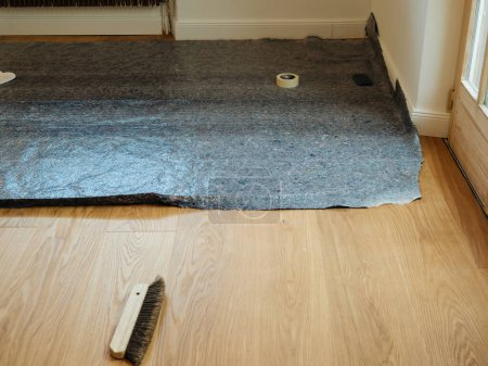 Téléchargez les photos : Revêtement d'un plancher de noyer nouvellement posé avec de la toison pour le protéger dans une maison en rénovation - en image libre de droit