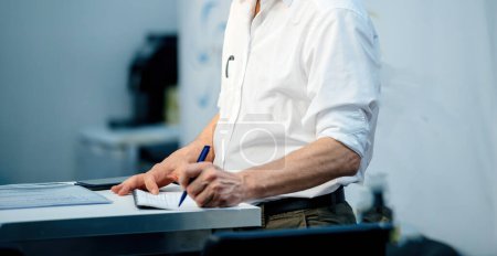 Foto de Un hombre de negocios en su oficina, bajo un elenco de color azul, firma un contrato de negocios crucial. - Imagen libre de derechos