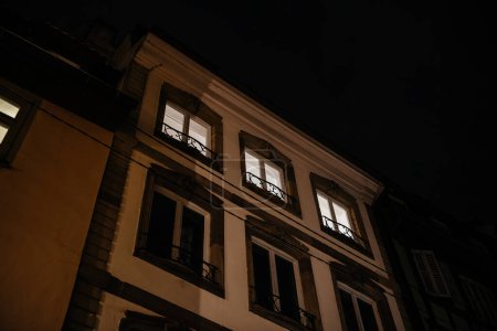 Windows aglow in a Haussmann-style building in France, depicting late-night activity