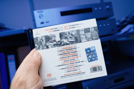 Foto de París, Francia - 28 de diciembre de 2023: Una mano masculina sostiene delicadamente Louise Rogers nueva SACD titulada Black Coffee, a jazz Super Audio Compact Disk. En el fondo, un sistema audiófilo de alta gama se muestra en - Imagen libre de derechos