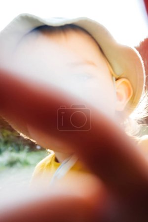 A young toddler holds his hands in front of the camera lens, symbolizing his understanding of privacy with a no photos please gesture