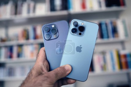 Photo for London, United Kingdom - Sep 29, 2022: A male hand holds the new titanium Apple iPhone 13 and 14 Pro smartphones against the backdrop of Vitsoe library shelves - Royalty Free Image