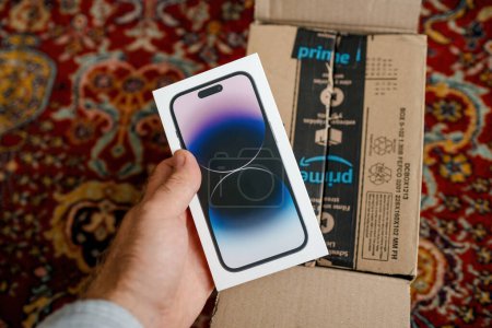 Photo for London, United Kingdom - Sep 29, 2022: POV of a male hand unboxing the latest Apple iPhone 14 Pro from an Amazon Prime cardboard box, set on a silky wooden rug. - Royalty Free Image