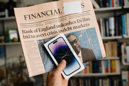 Téléchargez les photos : Londres, Royaume-Uni - 29 sept. 2022 : Une main masculine détient le dernier Apple iPhone 14 Pro tout en affichant le Financial Times, mettant en vedette les manchettes sur la Banque des glandes 57 milliards d'offres à - en image libre de droit