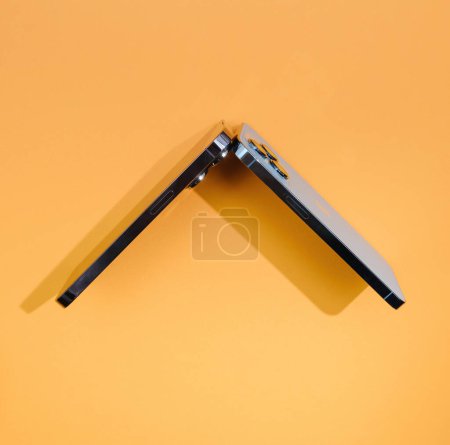 Photo for London, United Kingdom - Sep 29, 2022: Apples titanium-made smartphones, the 13 Pro and 14 Pro, are creatively arranged to form a rooftop shape against an orange background - Royalty Free Image