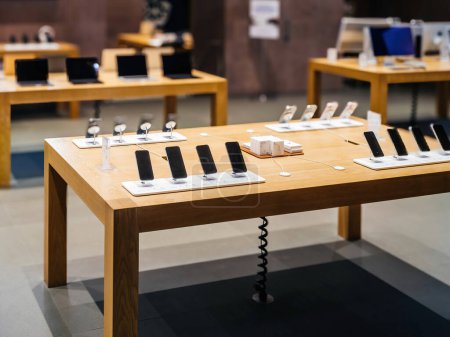 Photo for Paris, France - Dec 23, 2023: Tilt-shift lenses capture new Apple computers and iPhones on a desk inside an empty Apple Store, secured behind anti-vandal glass - Royalty Free Image