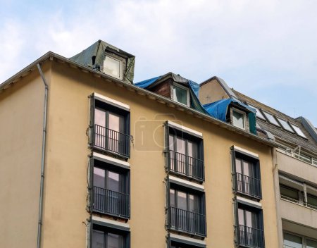 Fassade eines sanierungsbedürftigen Mehrfamilienhauses mit professioneller Isolierung, neu installierten Fenstern und einem reparaturbedürftigen Dach.