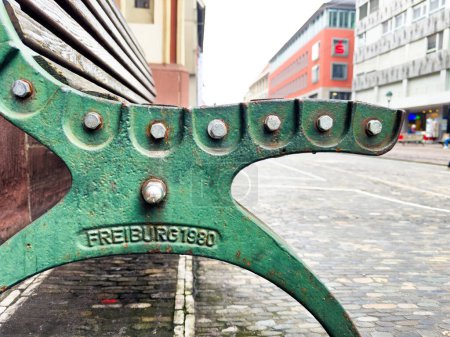 A steel public bench in Freiburg displays 1980 signage, with classic German architecture in the background.