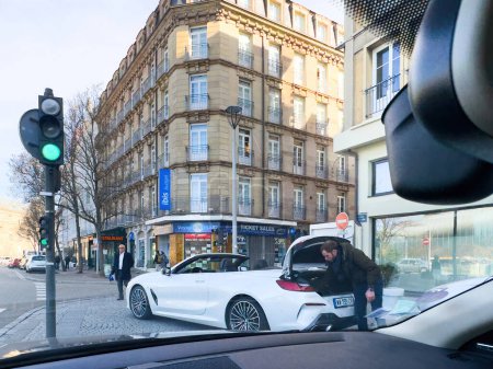 Photo for Strasbourg, France - Mar 9, 2024: View from a BMW Cabrio showing a man searching the trunk for luggage in front of a Strasbourg hotel. - Royalty Free Image
