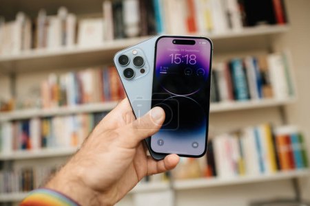 Photo for London, United Kingdom - Sep 29, 2022: A male hand presses the latest Apple iPhone 14 Pro while comparing it to the iPhone 13 Pro, with Vitsoe shelves in the defocused background, highlighting the - Royalty Free Image
