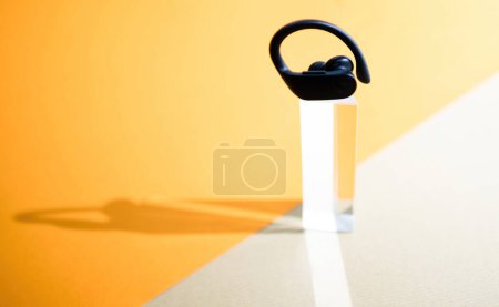 Téléchargez les photos : Londres, Royaume-Uni - 29 sept. 2022 : Un écouteur sans fil Powerbeats Pro de Beats, debout sur un piédestal clair sur un fond orange, soulignant son design élégant et son héros de forme ergonomique - en image libre de droit