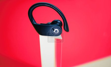 Téléchargez les photos : Londres, Royaume-Uni - 29 sept. 2022 : Un écouteur sans fil Powerbeats Pro de Beats s'affiche bien en évidence sur un piédestal clair, placé sur un fond rouge vif, mettant en valeur son design sophistiqué et - en image libre de droit
