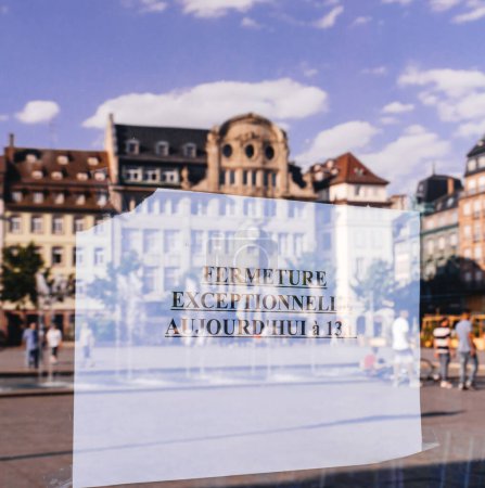 Téléchargez les photos : Un panneau en papier sur une fenêtre de magasin annonce aujourd'hui une fermeture exceptionnelle à 13 heures, avec la magnifique architecture de la ville reflétée en arrière-plan, créant un mélange d'historique et - en image libre de droit